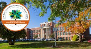 A large brick academic building with white columns is surrounded by trees and parked cars; a “Carnegie Foundation Elective Classification” badge overlays the image.