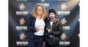 Two people stand in front of a step-and-repeat banner that reads “Wortown Rising,” both smiling and pointing at each other.