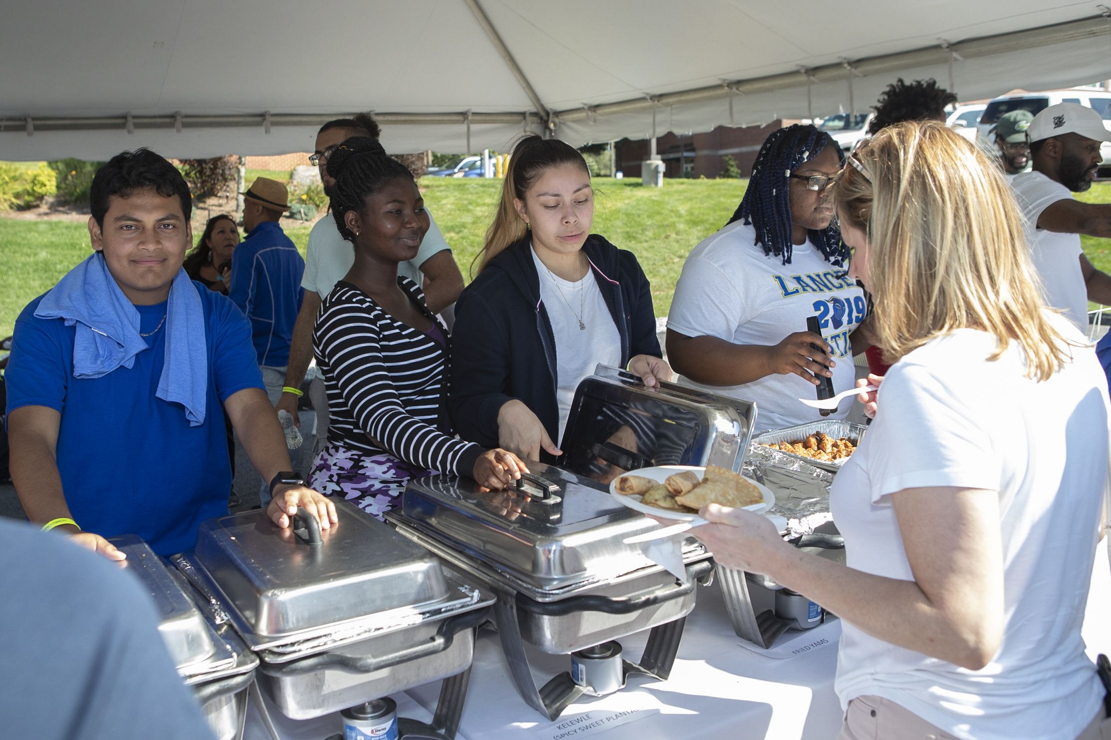 Students serving each other food under a tent outside during homecoming