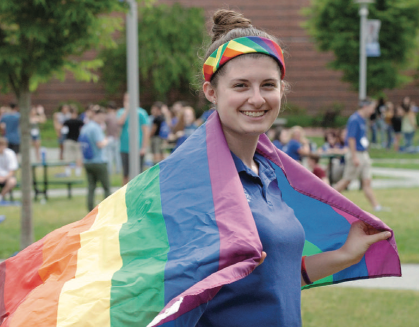 A Worcester State student wearing a pride flag on their shoulders like a cape