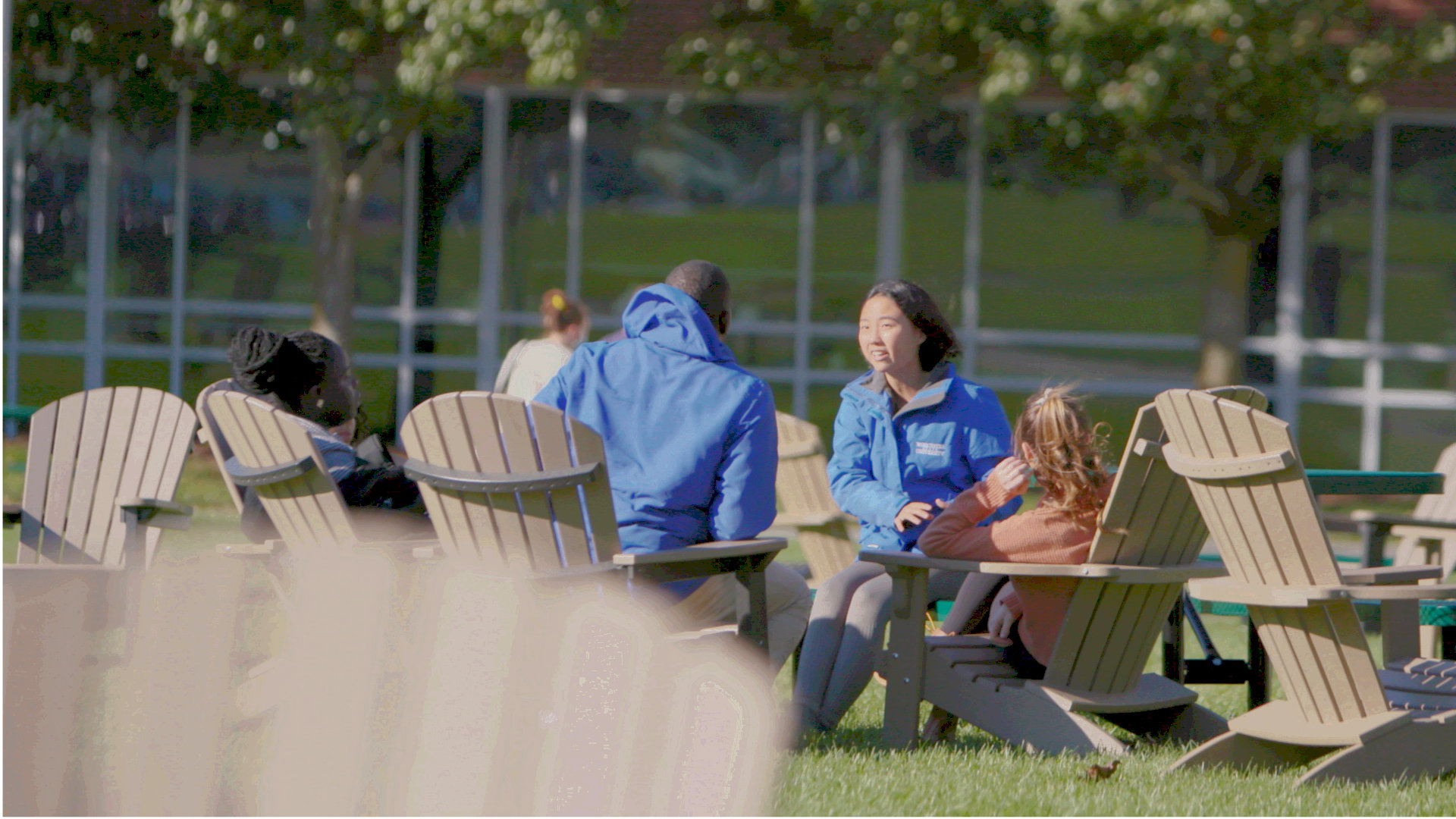 Worcester state students sitting in Adirondack chairs outside on campus