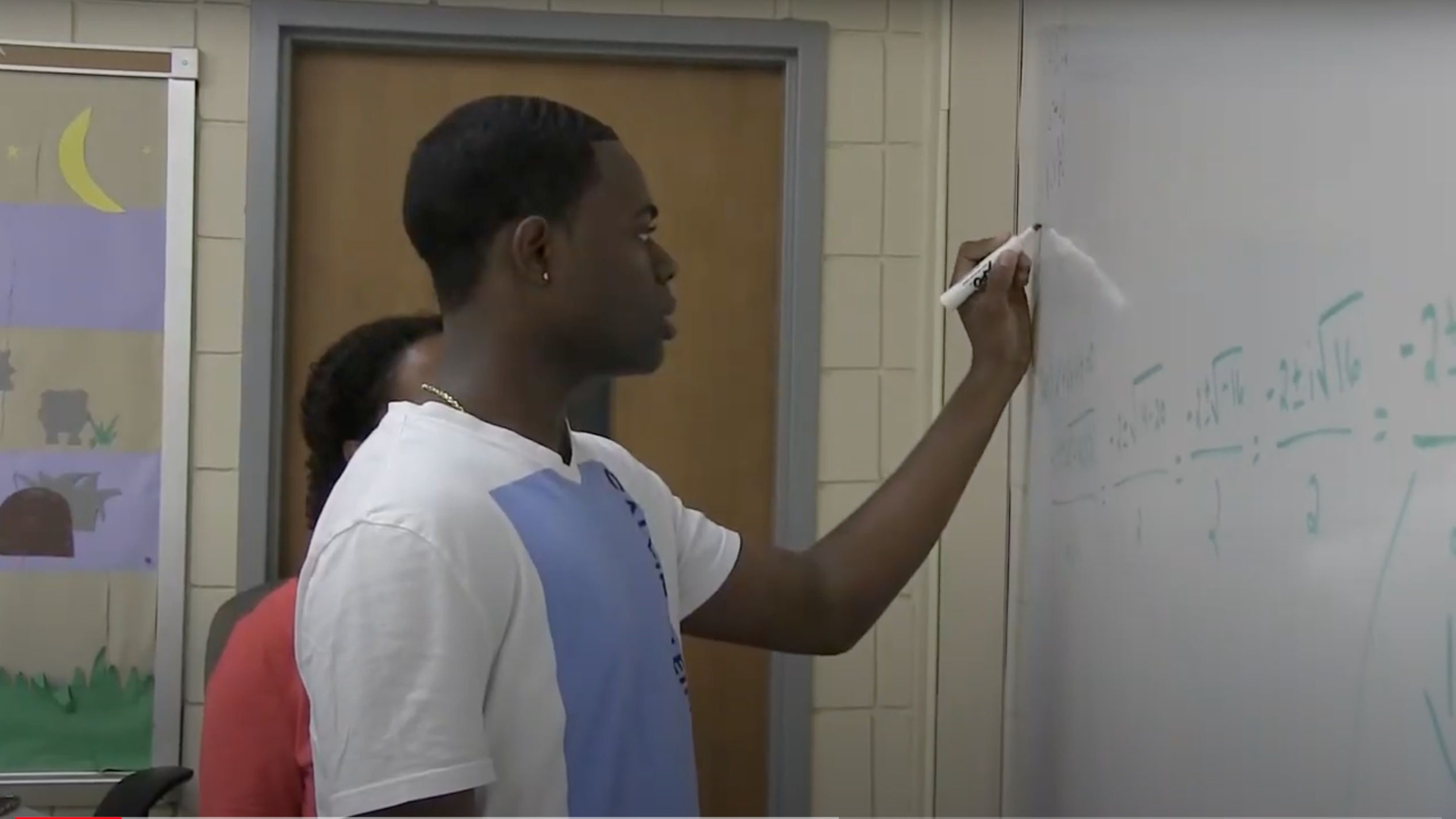 Student writing with a marker on a whiteboard in a classroom