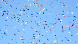 Colorful confetti pieces are scattered and falling against a clear blue sky.