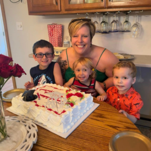 A woman and three children sitting at a wooden table with a graduation cake.