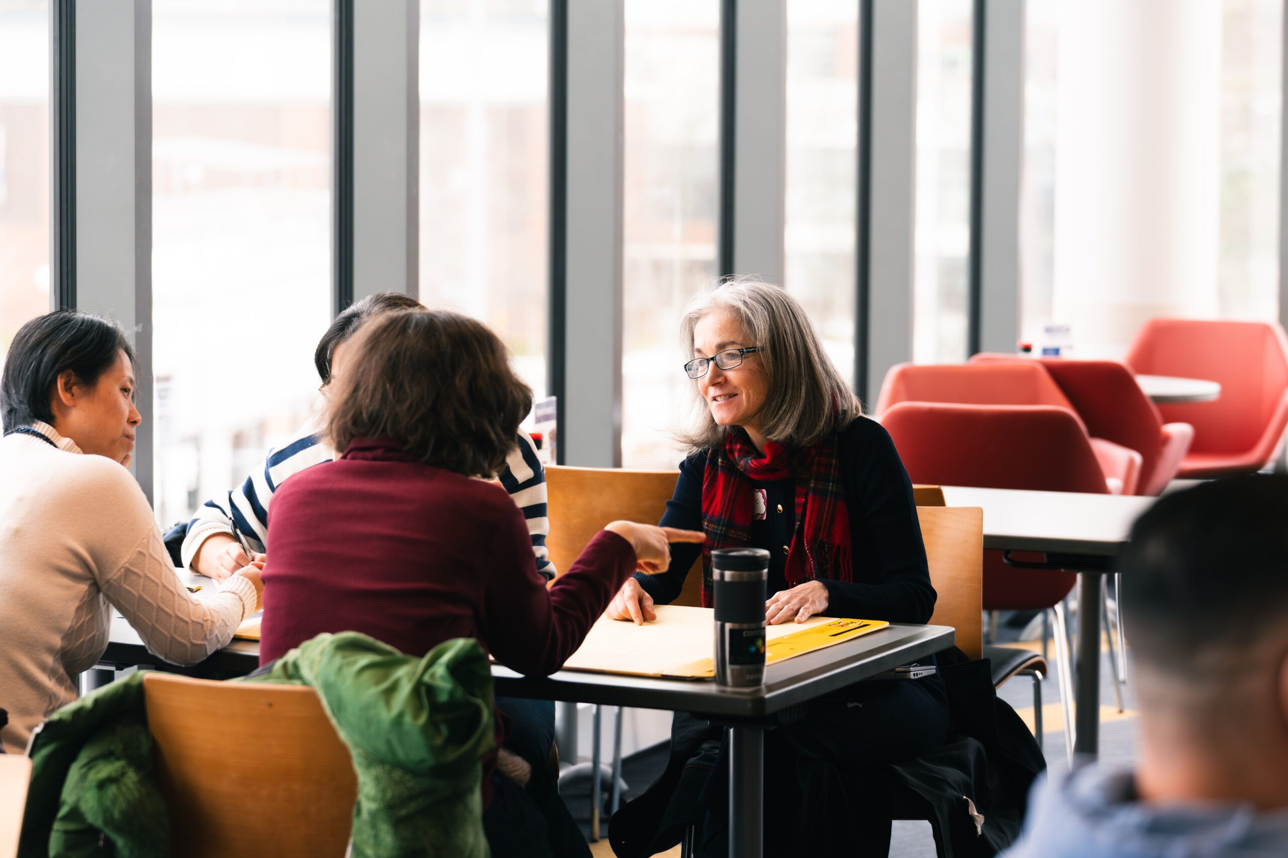 Group at a table, one woman speaks to the rest, gesturing.