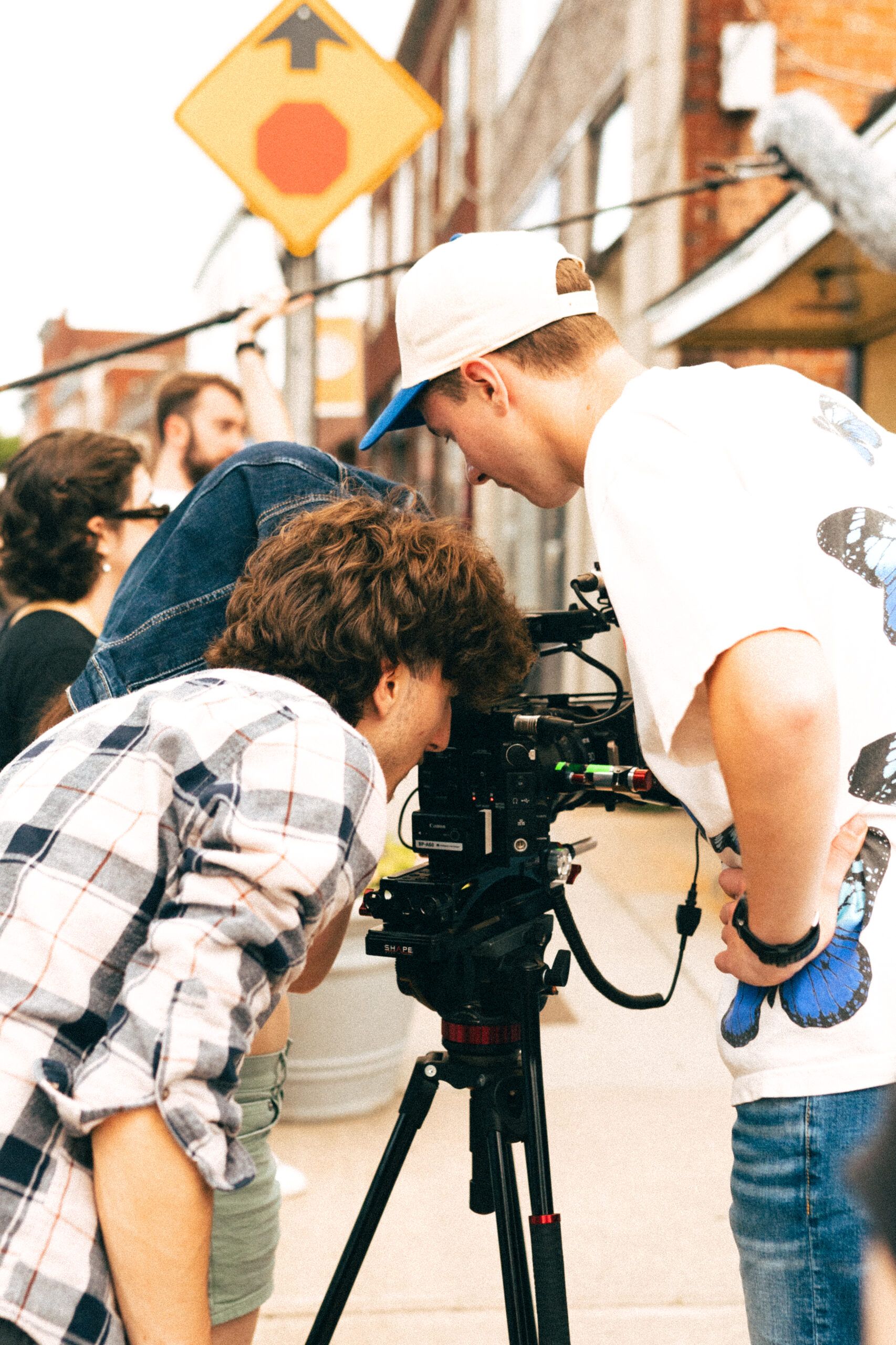 Two people examine a camera on a tripod outdoors, on a film set.