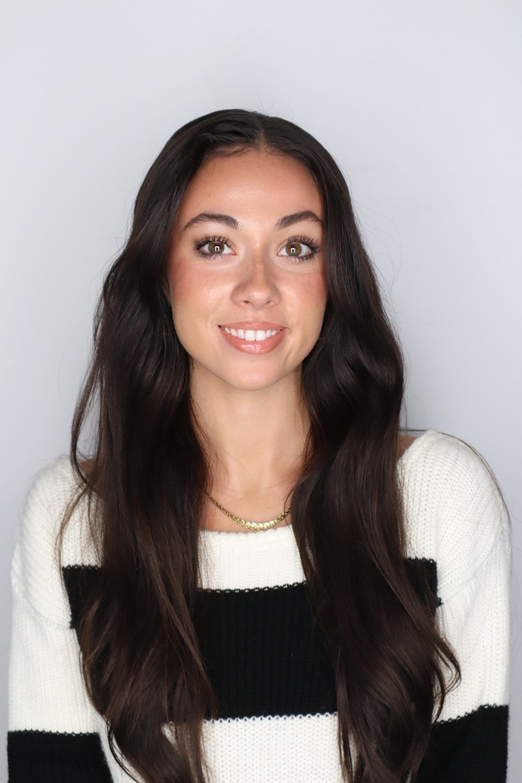 Photo of smiling woman with dark hair wearing a black-and-white striped sweater against a plain white backdrop.