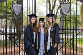 Three students in graduation gowns in front of Worcester State gates