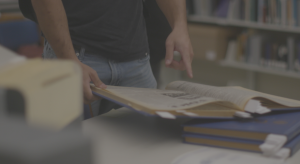 History student at worcester state points at a page in an historic text in the Worcester Archives