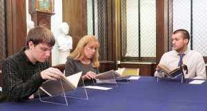 3 Worcester State University History Students sit at a table with antique books in plastic holders, conducting research at American Antiquarian Society