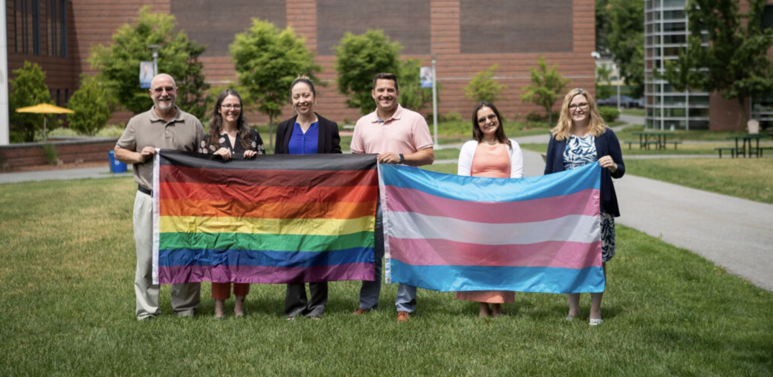 Folks holding up inclusive LGBTQ+ & Trans flags