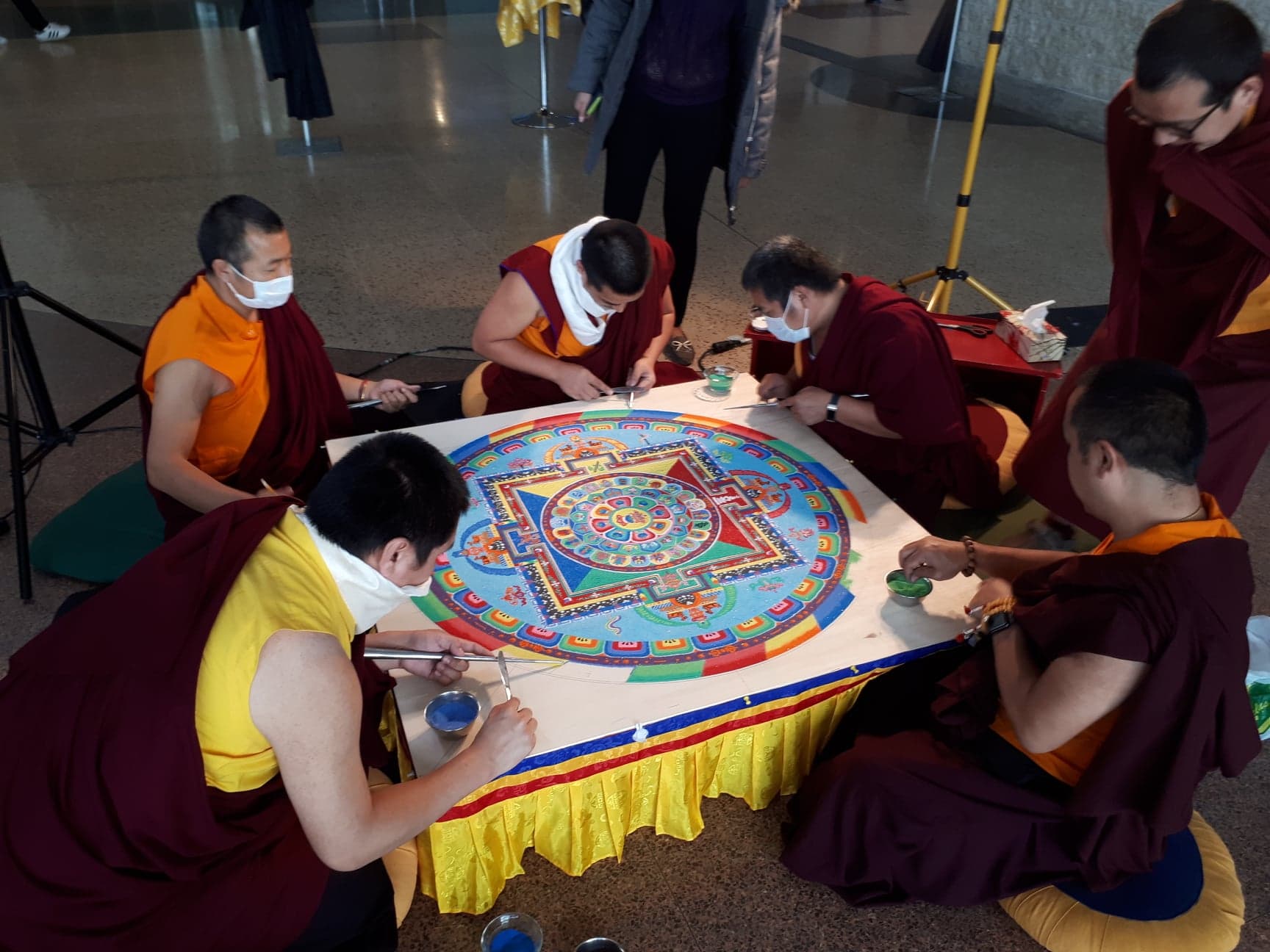 Five monks seated at a low table assemble a colorful sand mandala