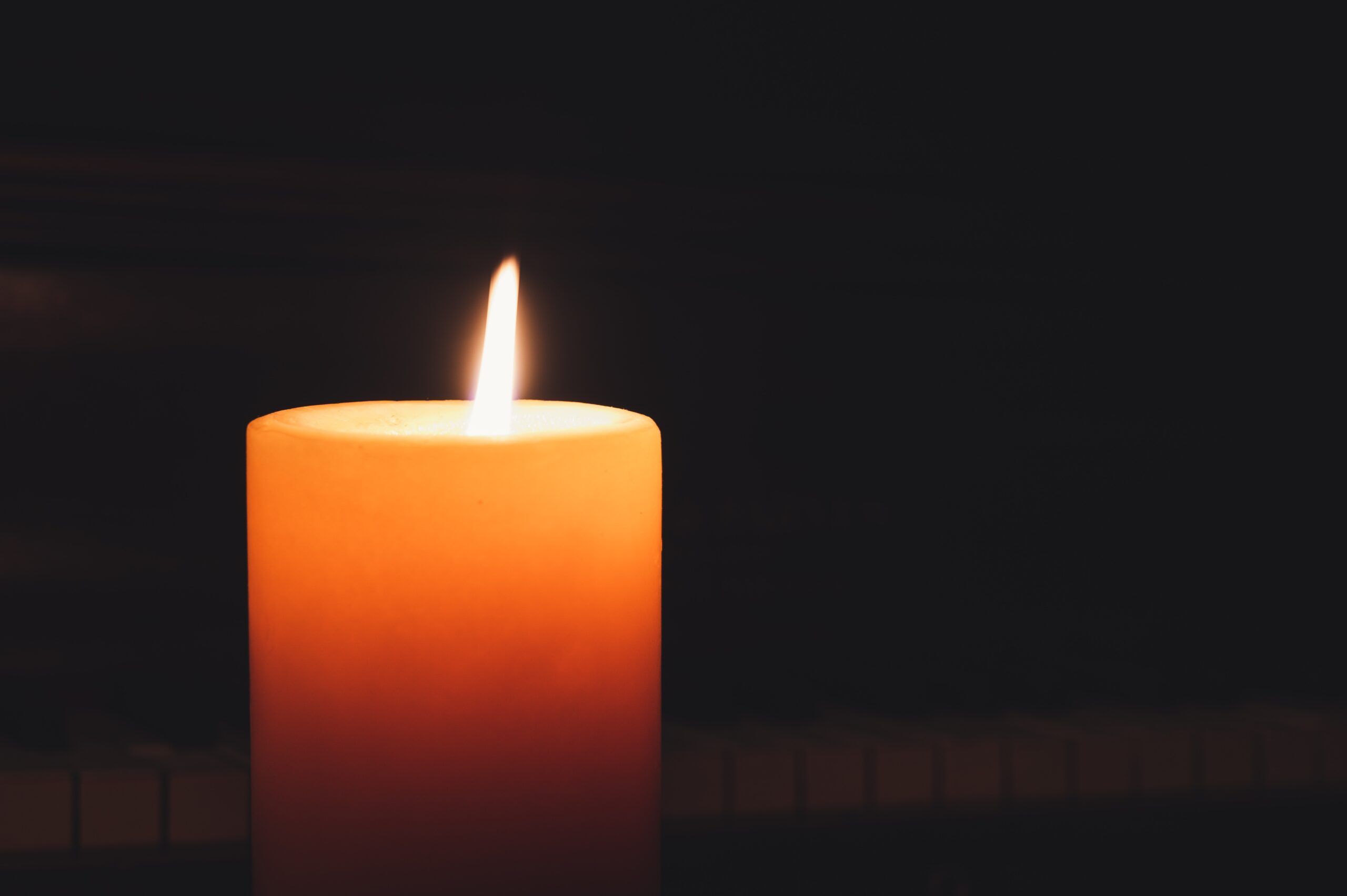 A lit white candle in darkness
