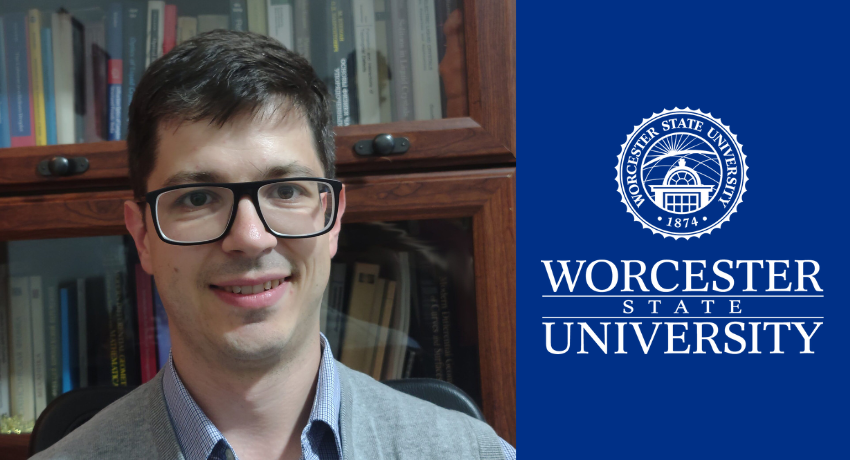 A man wearing glasses and a gray sweater smiles in front of a bookshelf, next to the Worcester State University logo on a blue background.