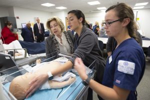 Nursing presentation in simulation lab, student checks the vitals of a model baby as faculty watch