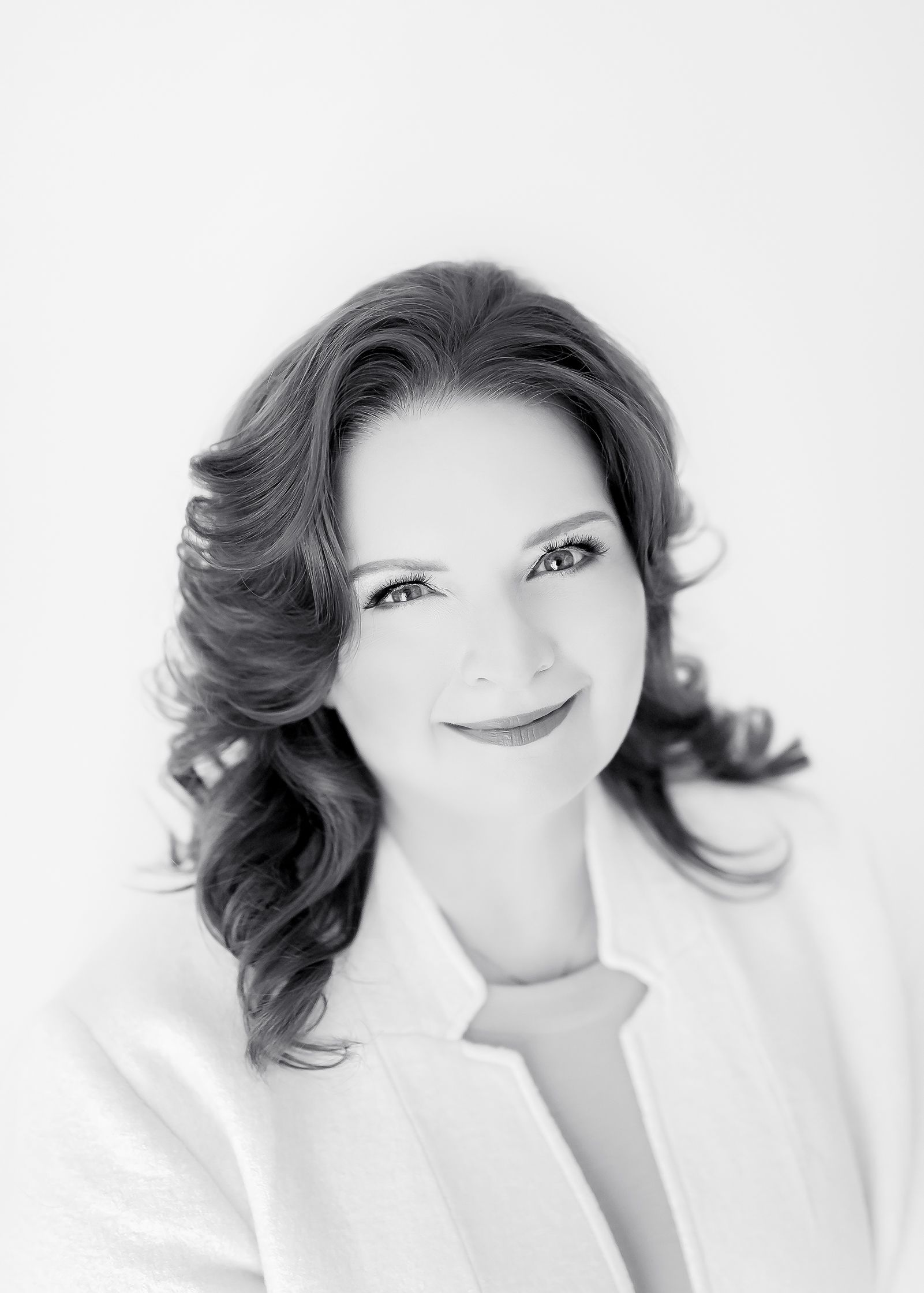 Black and white headshot of a person with wavy hair, wearing a light-colored top, smiling at the camera.