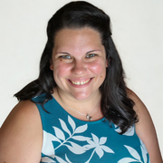 A woman with long dark hair and a blue sleeveless top with white leaf patterns smiles at the camera against a plain light background, reflecting the spirit of University Advancement.