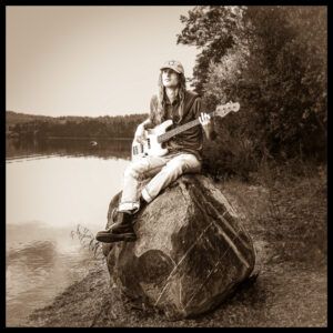Julian Wagner poses on top of a rock with his guitar.