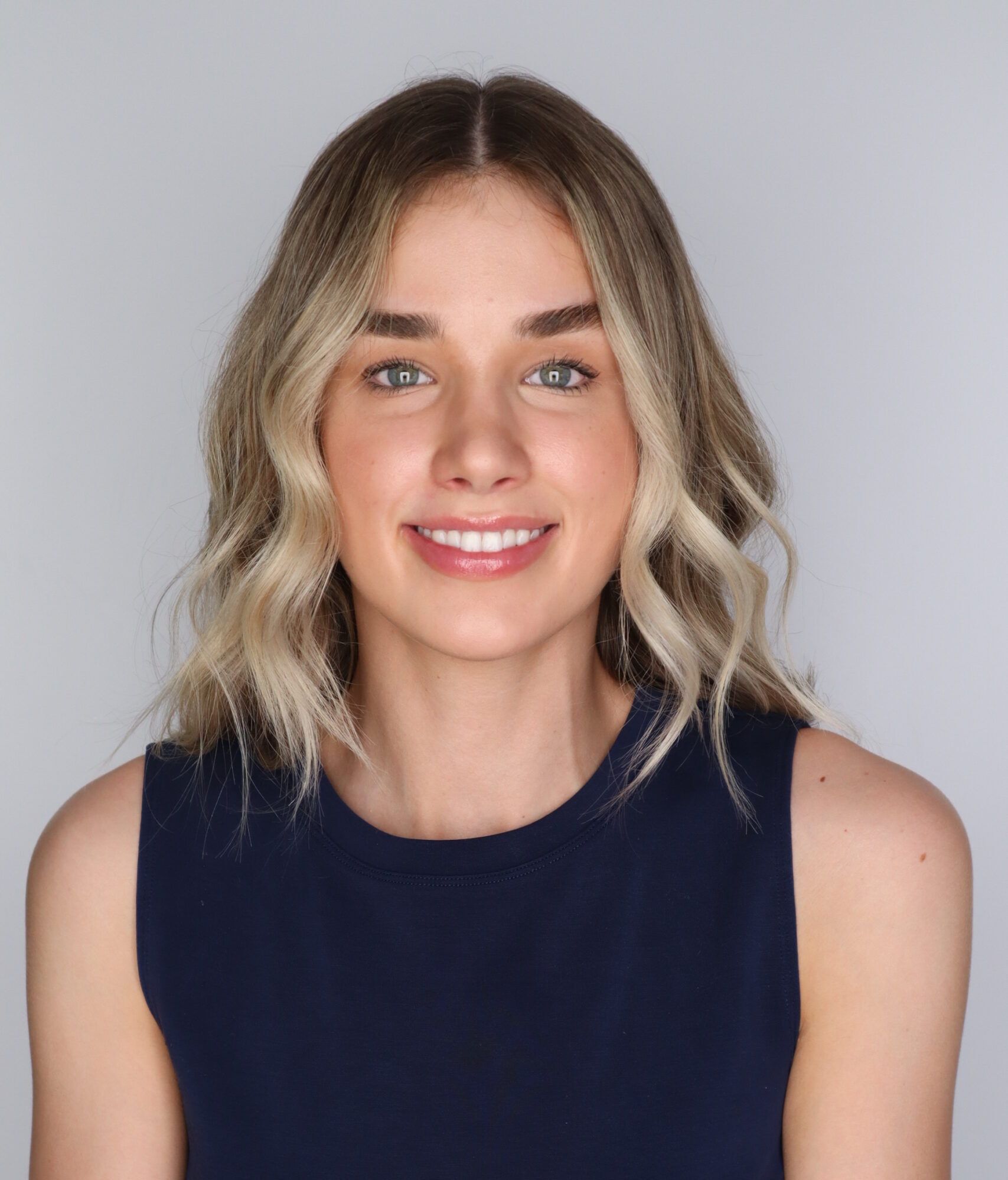 A woman with shoulder-length blonde hair wearing a navy blue sleeveless top, reflecting her master of occupational therapy.