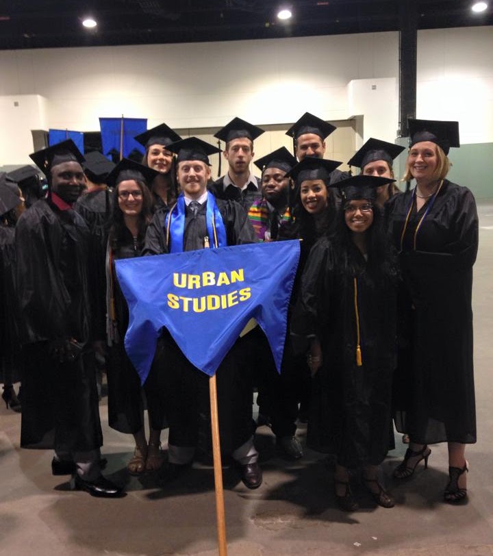 Students holding up a banner that states "Urban Studies" at graduation