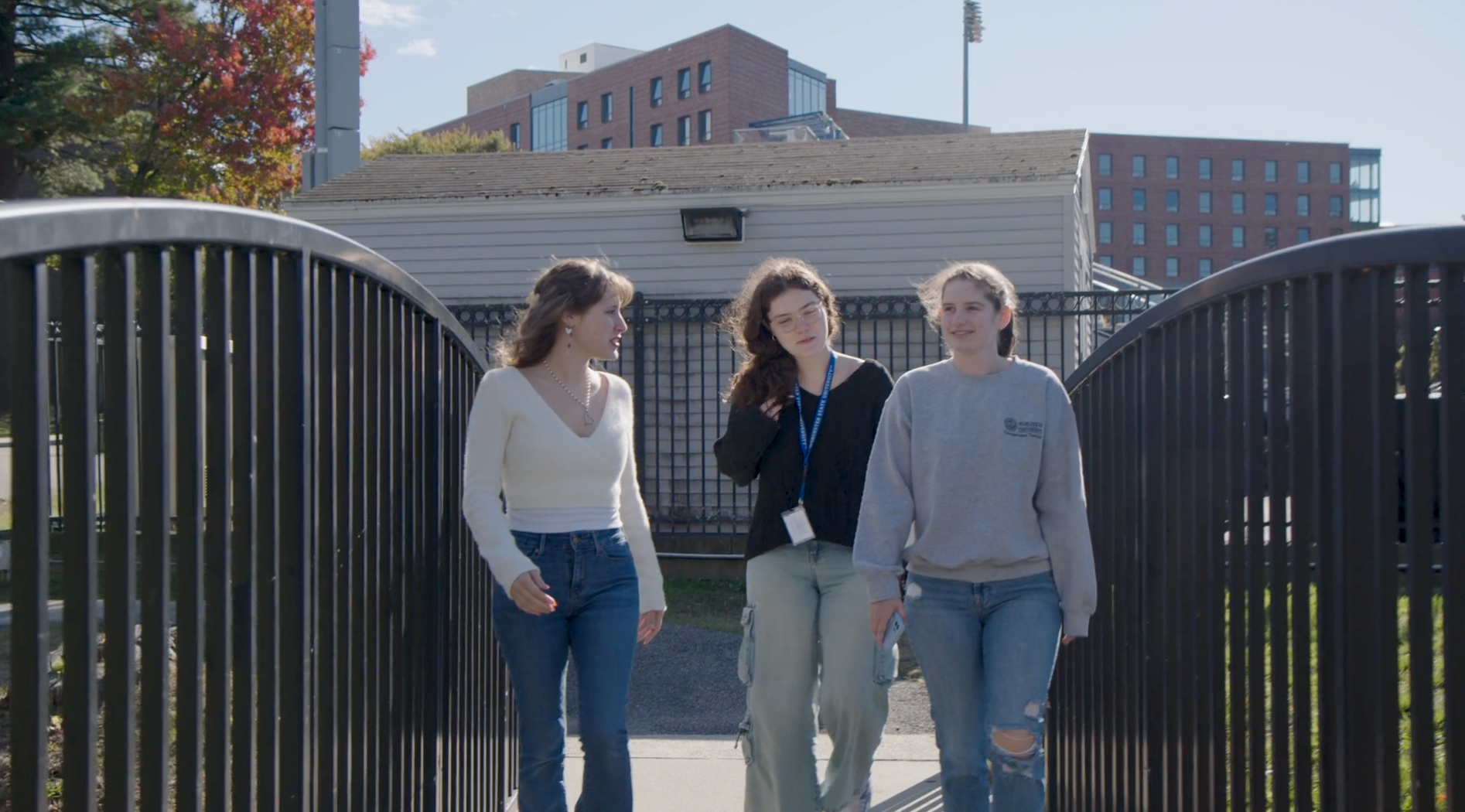 Three young women, all Communication Sciences and Disorders majors, walk together outdoors on a sunny day, with buildings and a fence visible in the background.