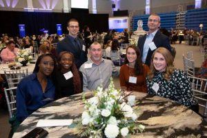 A group of Worcester State alumni sitting at a table smiling for a photo