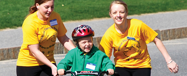 Two Worcester state students helping a small child learn how to ride their bike