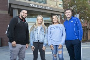 A group of 4 Worcester State students standing in front of Wasylean Hall on campus