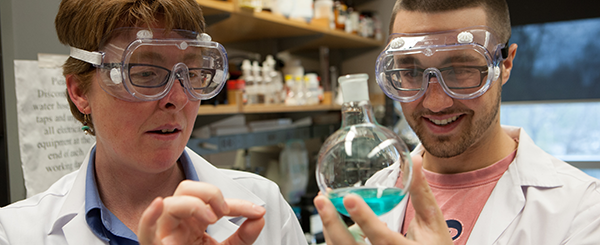 A chemistry students and professor looking at a chemical in a science lab