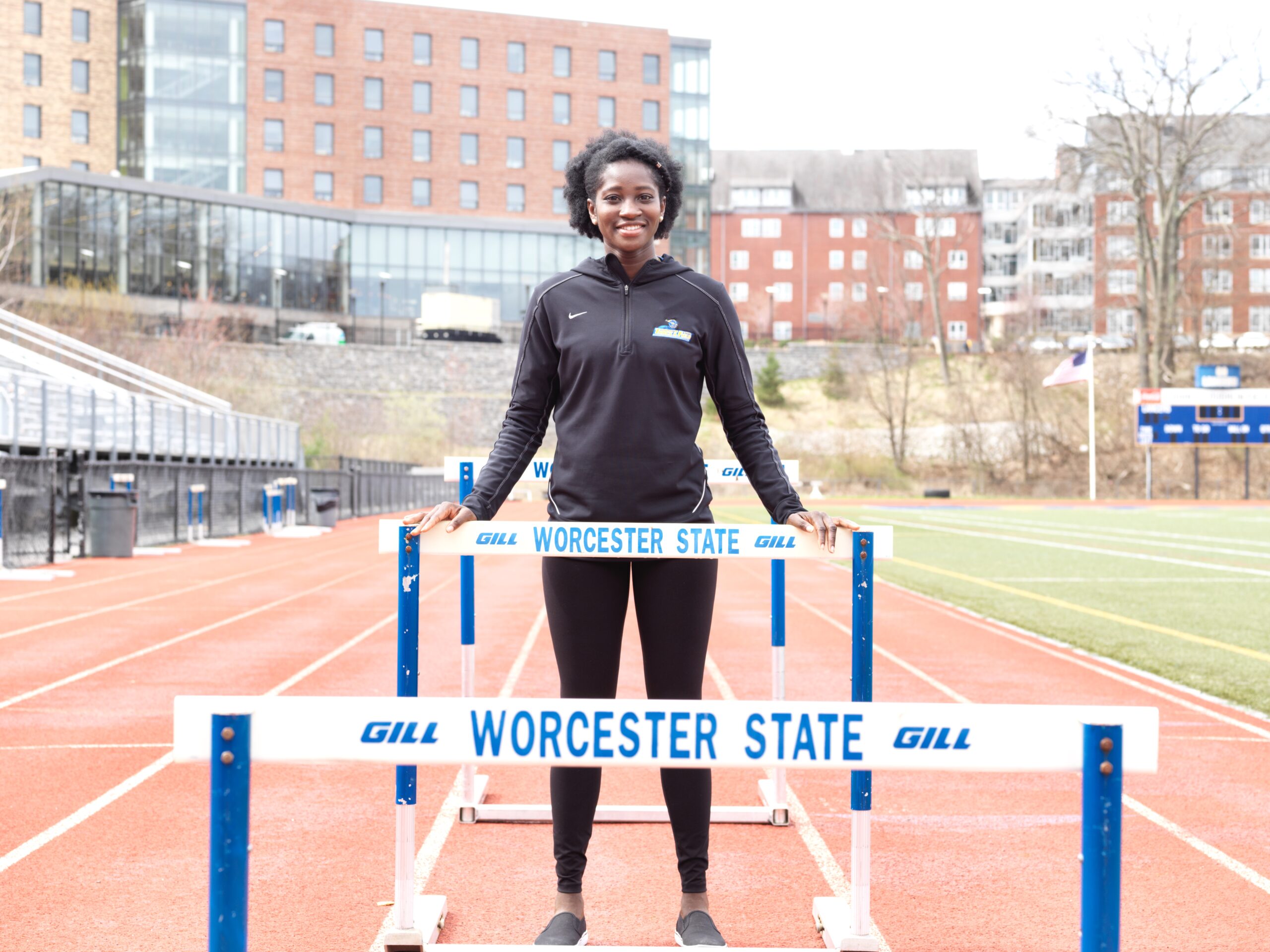 A Worcester state track athlete standing next to equipment that reads Worcester State