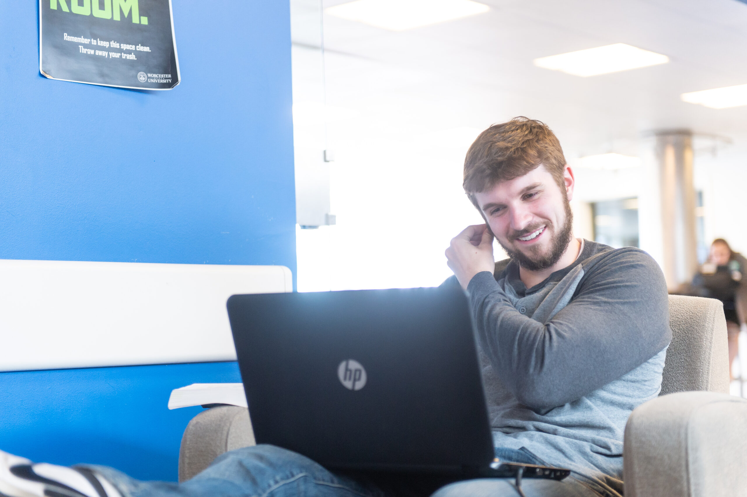 A Worcester State student smiling while looking at their laptop in a shared study lounge