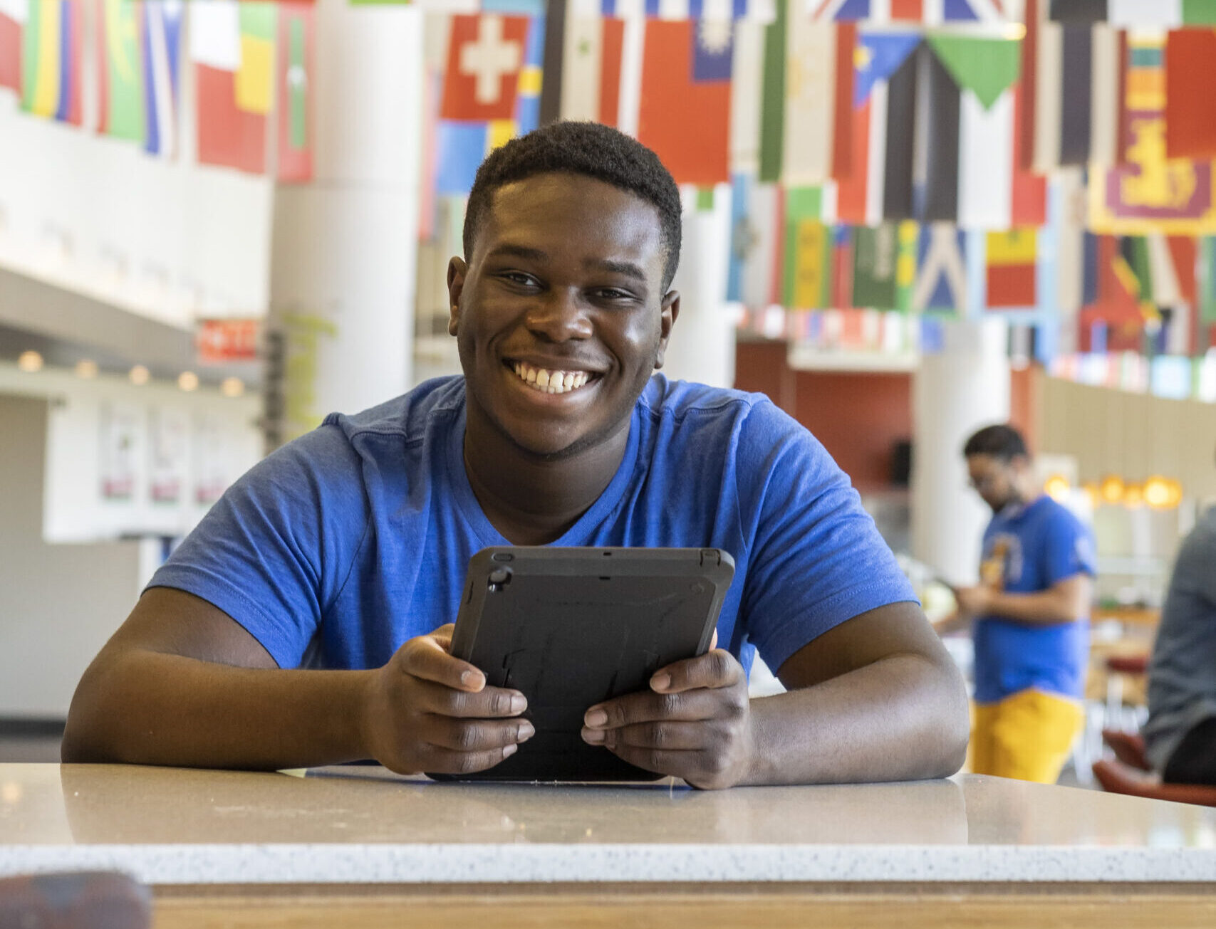 A smiling Worcester State student on an iPad in the dining hall