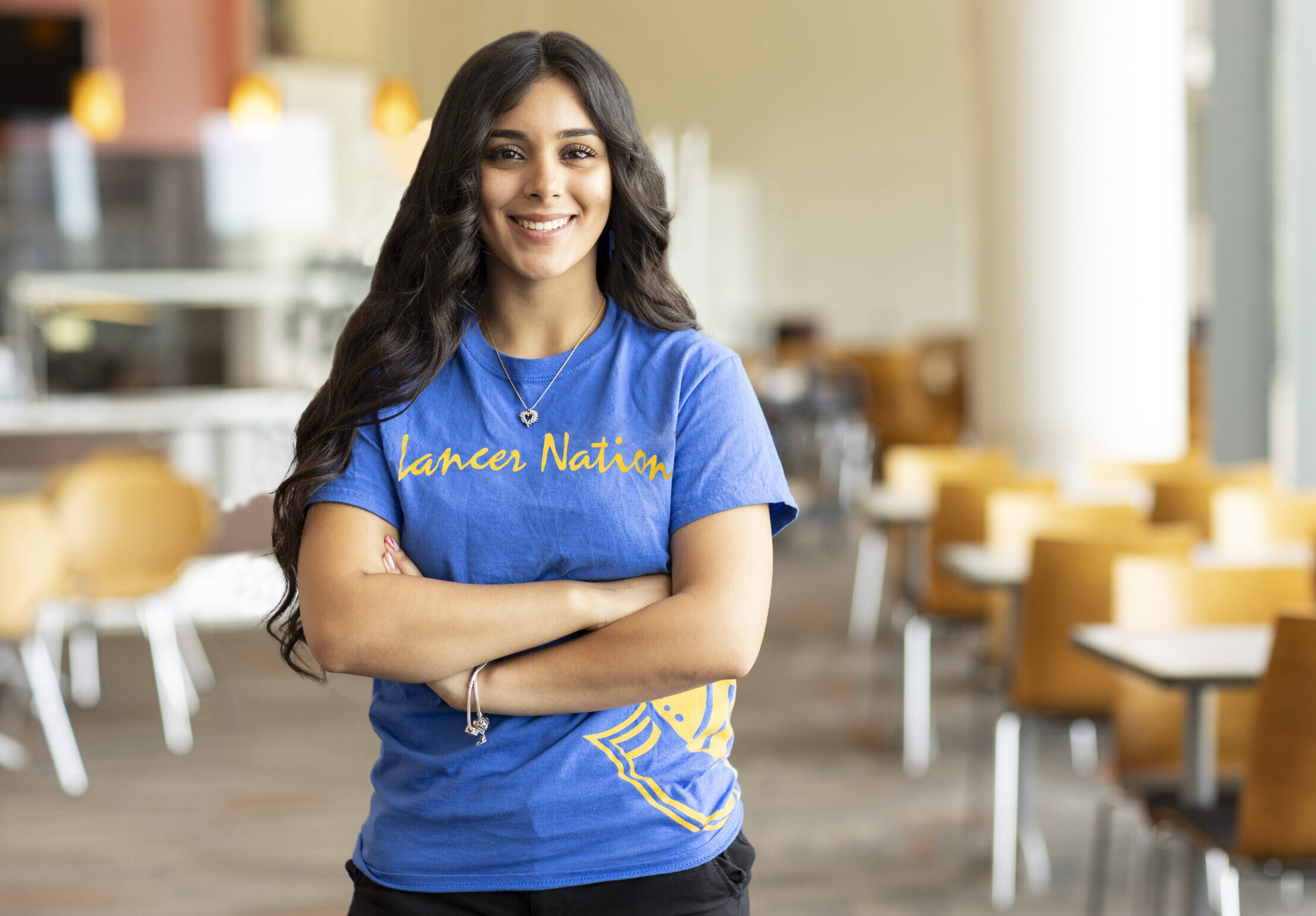A smiling student in the Worcester state dining hall wearing a shirt that reads Lancer Nation