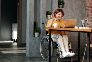 A person in a wheelchair at a desk, meeting virtually on a laptop with headphones