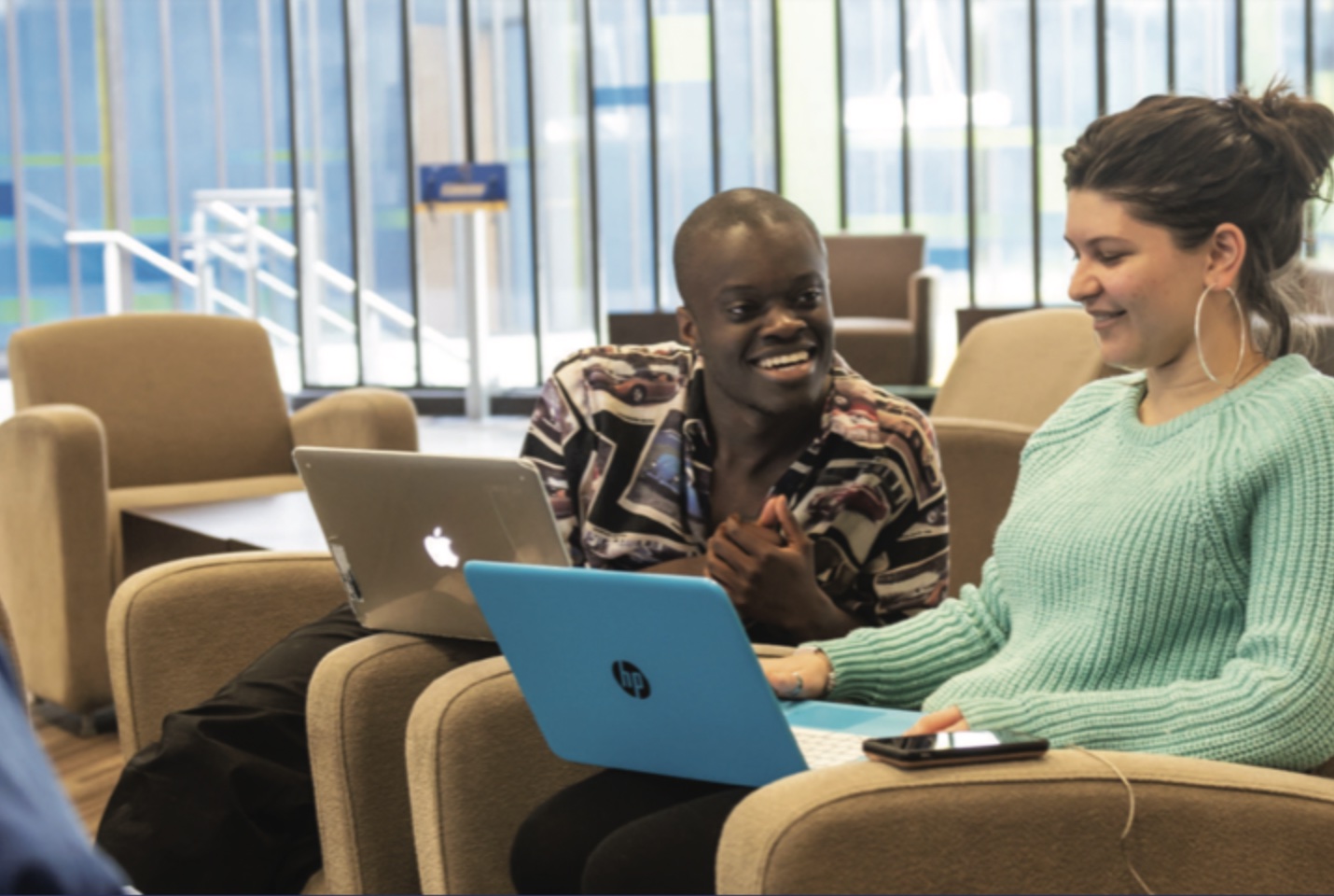 Two students working together on laptops in a communal lounge on campus