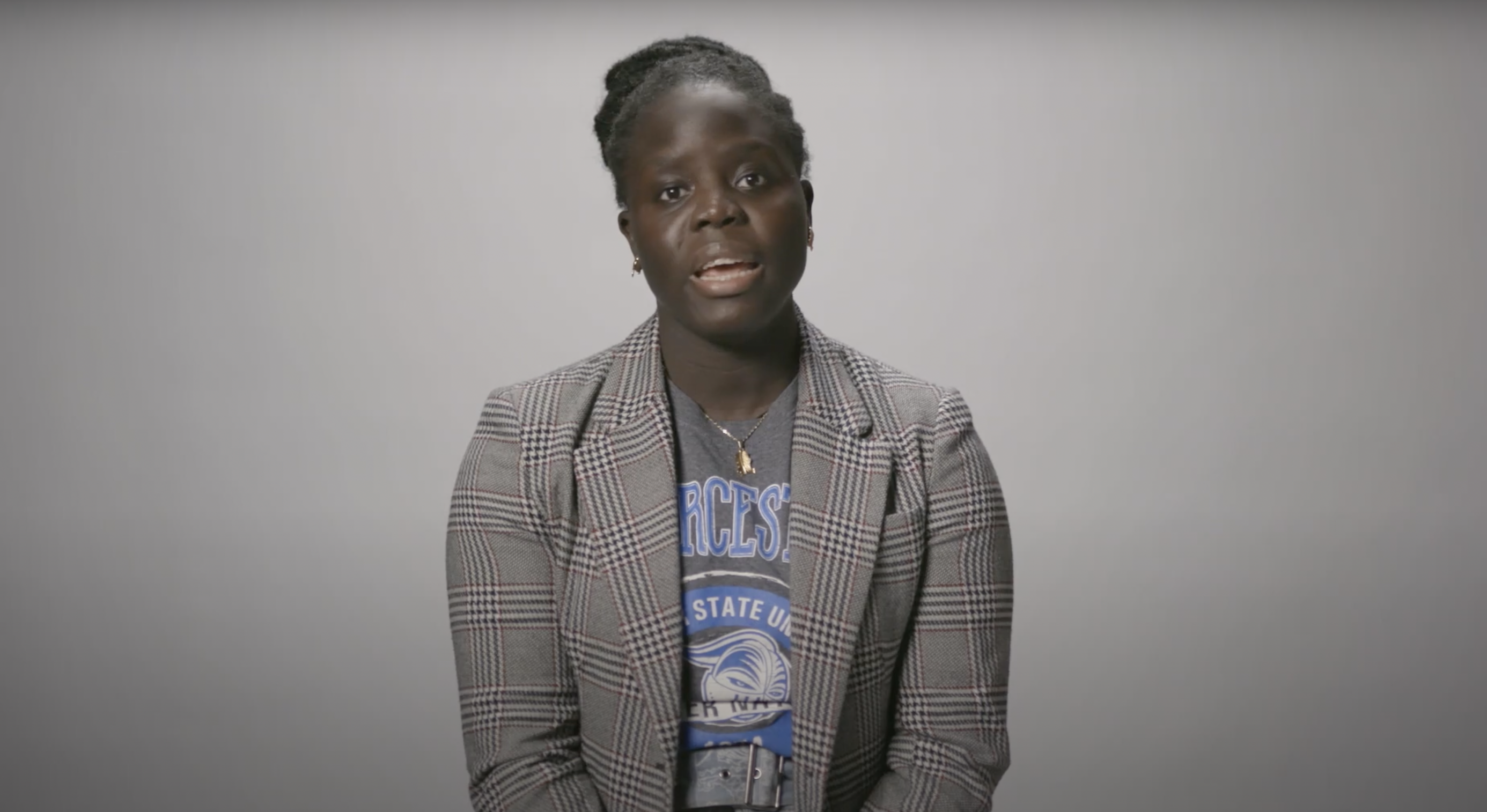 Woman in a checked blazer over a university t-shirt speaking to the camera.