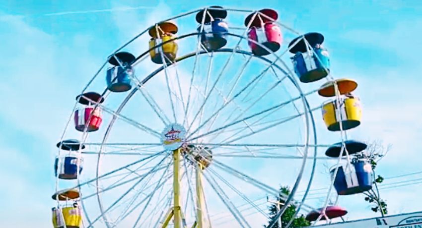 A Ferris wheel with colorful passenger cabins stands majestically against a blue sky, reminiscent of the vibrant spirit found at Worcester State University.