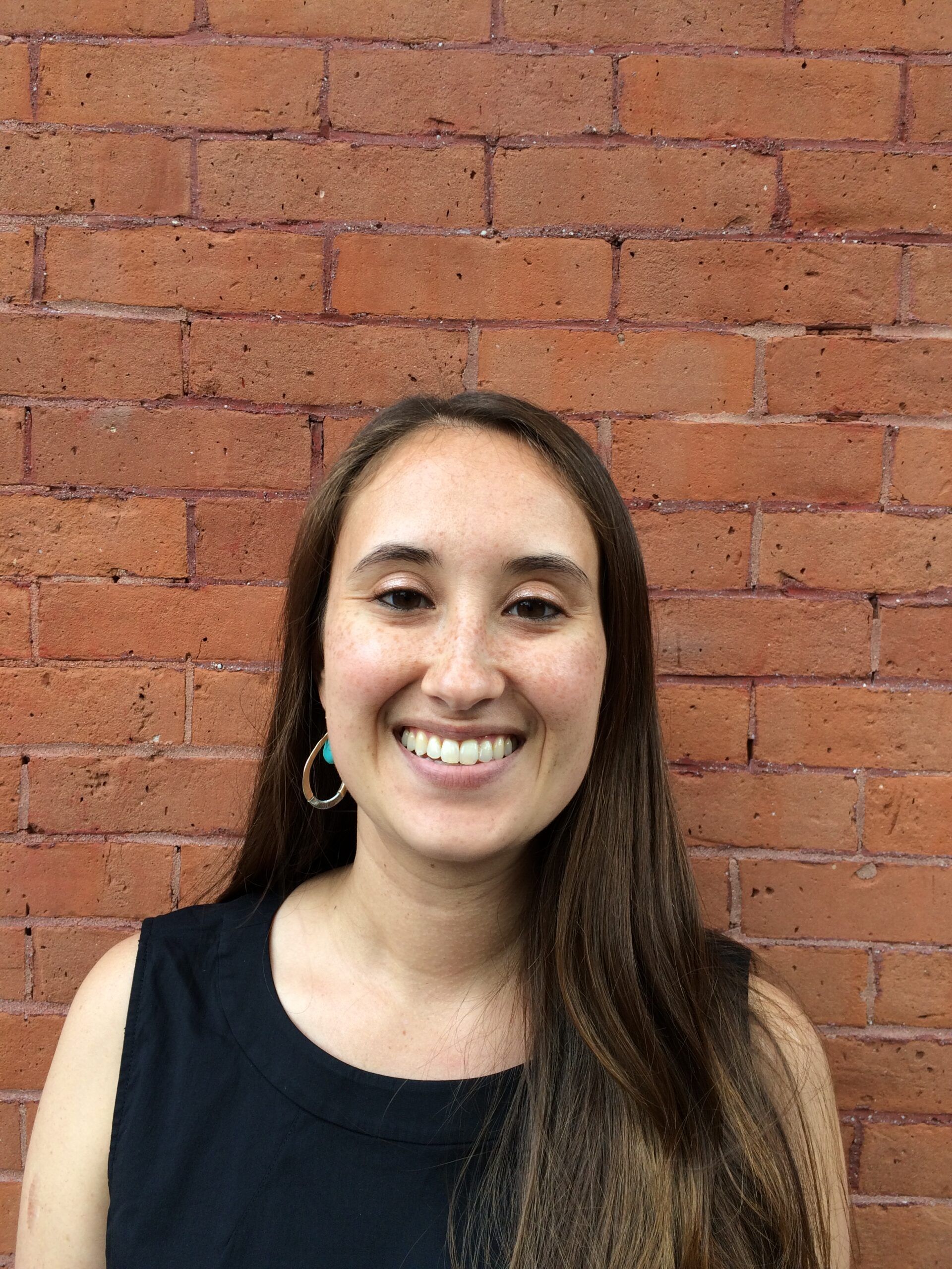 Woman with long hair smiling, standing in front of a brick wall.