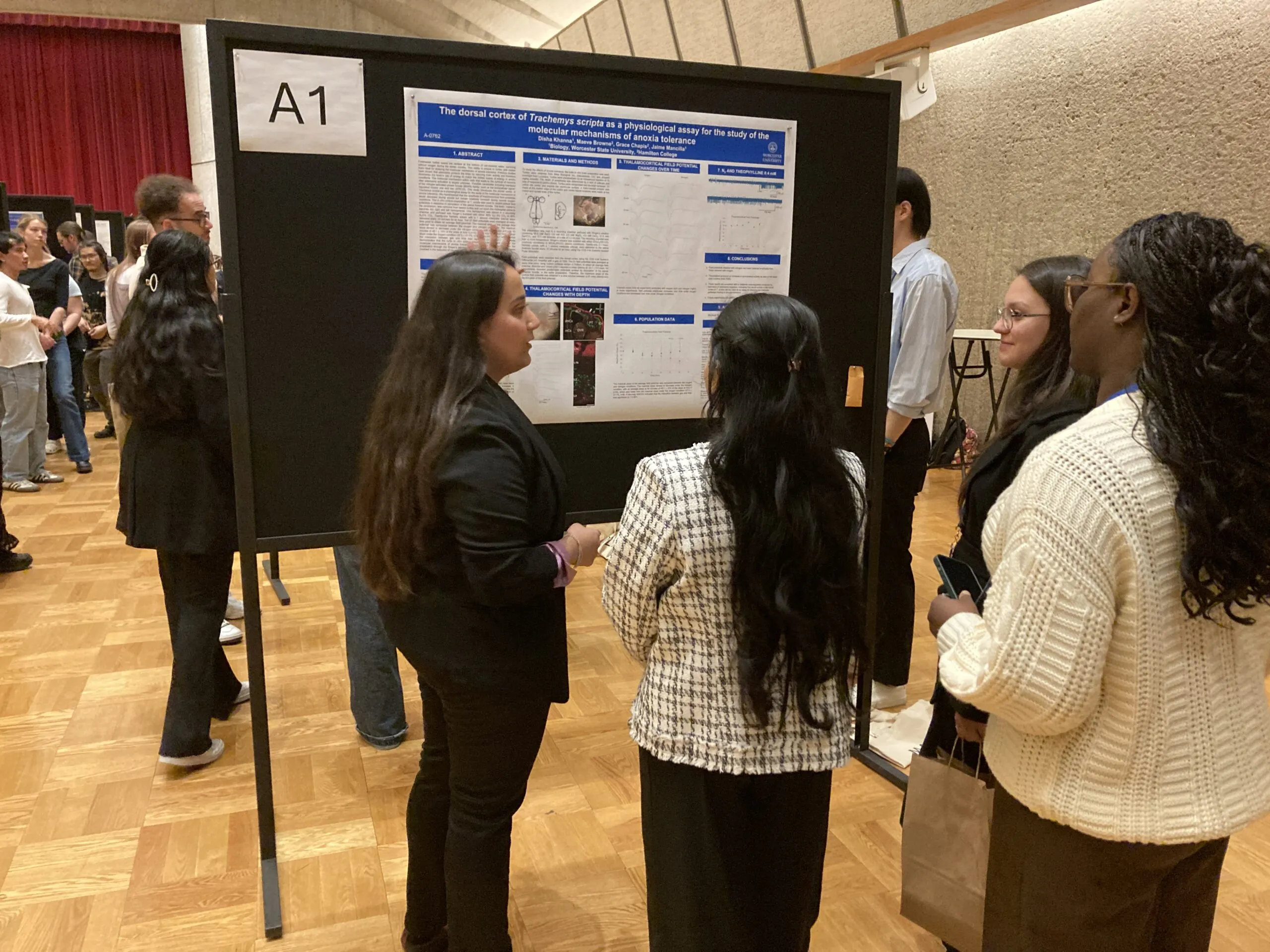 Several people stand in front of a scientific research poster on display at an academic conference, discussing its content in a large indoor room.