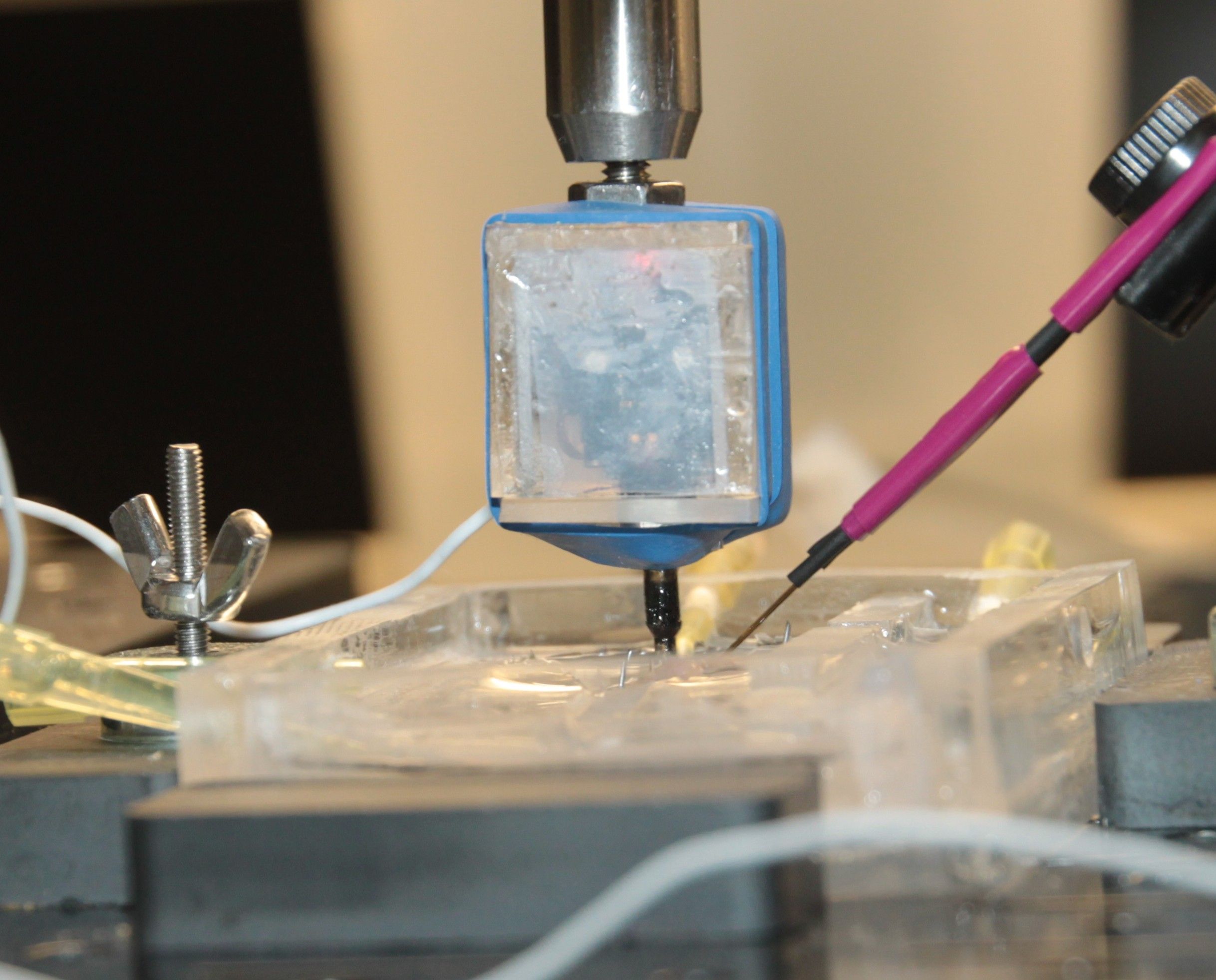 Close-up of laboratory equipment with electrodes and wiring set up on a transparent platform, possibly for an experiment involving precise measurements or testing.