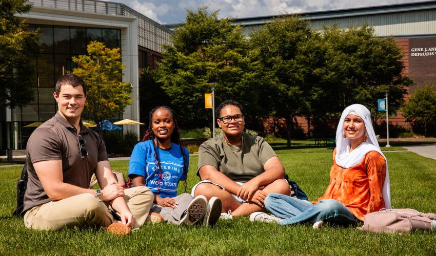 Four students sitting on the Worcester State University lawn in front of a campus building.