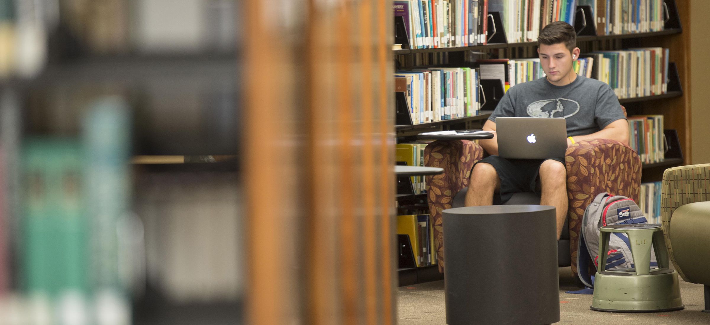 A student sitting in a library armchair, using a laptop.